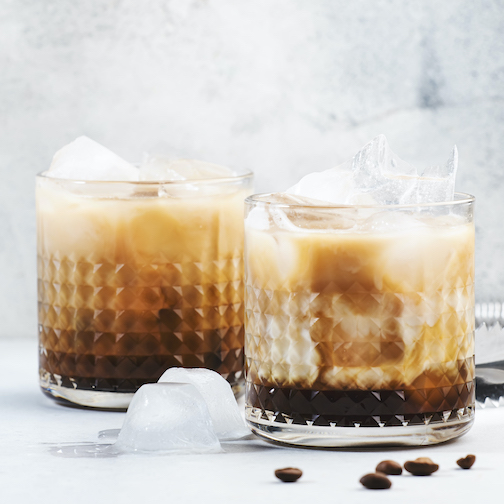 Close-up of drinks on table White russian cocktail, trendy alcoholic drink with vodka, coffee liqueur, cream and ice, gray background, bar tools